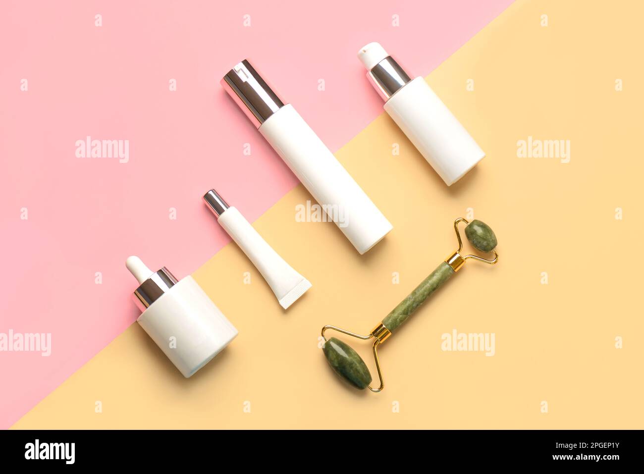 Set di cosmetici e rullo massaggiatore in giada per la cura della pelle su sfondo giallo e rosa. Concetto di prodotti per la cura della pelle Foto Stock