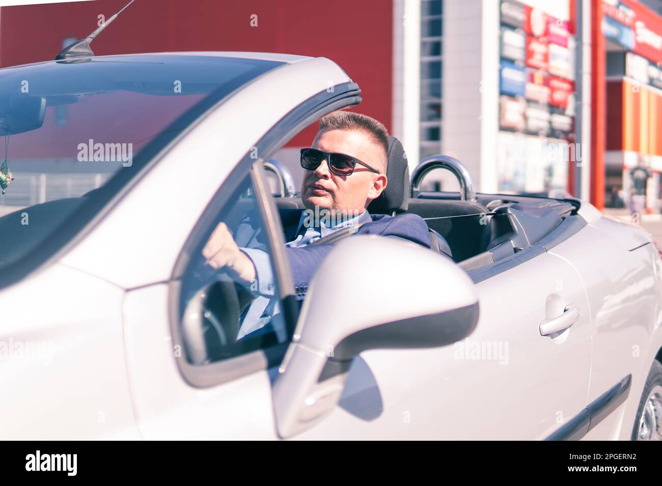 Uomo elegante seduto in auto sportiva. Un uomo d'affari di successo guida una costosa auto convertibile in giro per la città durante il giorno. Foto Stock