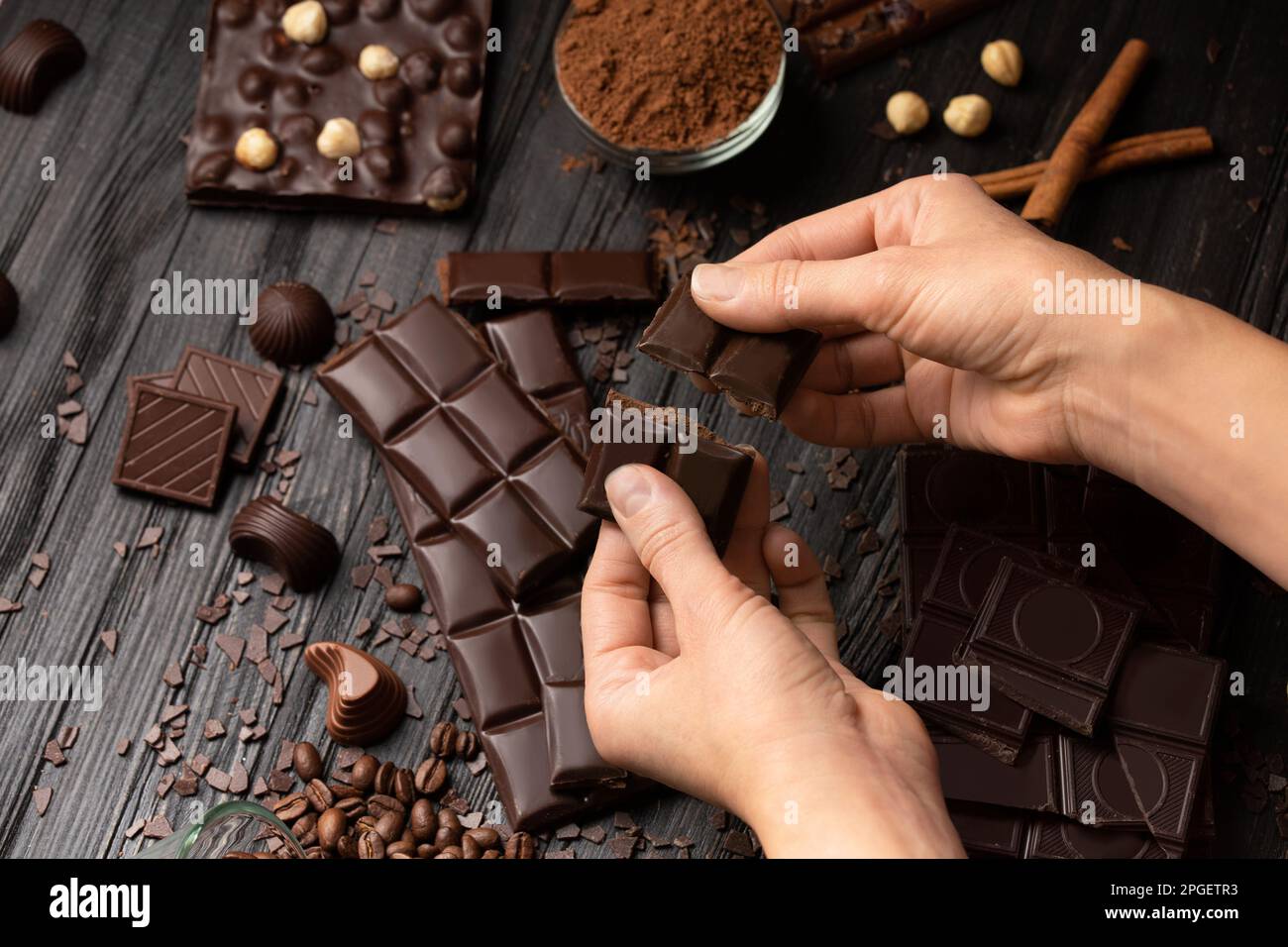 Piatto di cioccolato su sfondo di legno scuro. Dessert al cioccolato in mani femminili su uno sfondo di cioccolato fondente e al latte sparso. Foto Stock