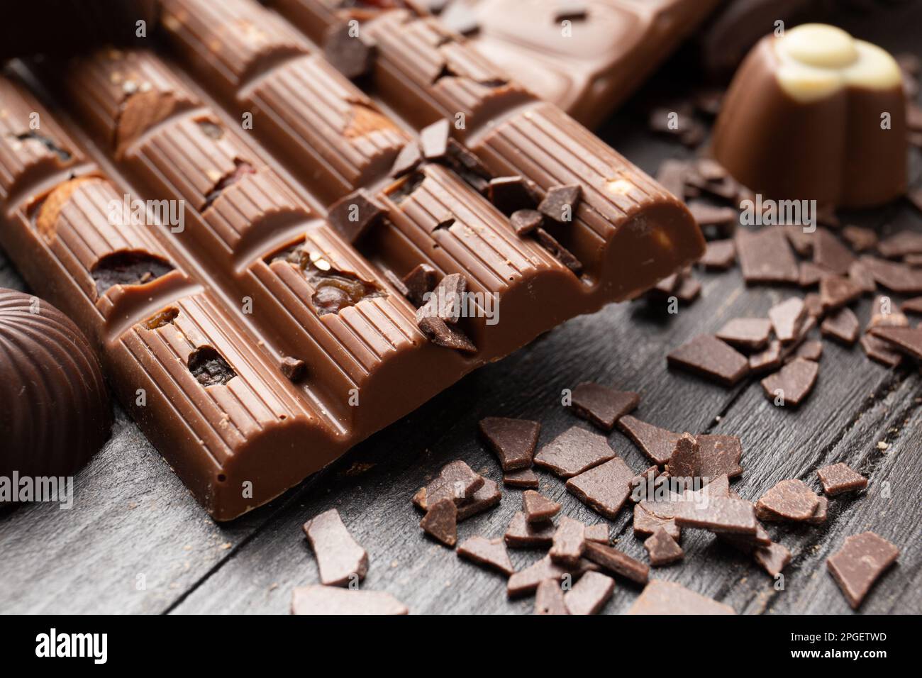 Cioccolato fatto a mano rotto con gocce di cioccolato e dolci su uno sfondo scuro primo piano. Una barretta di cioccolato con uva passa e noci Foto Stock