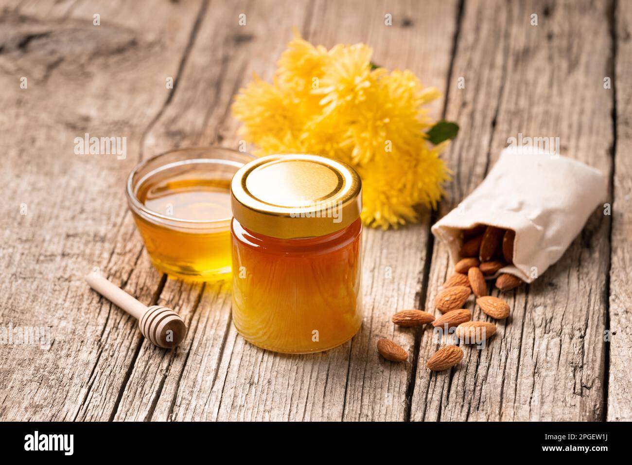 Miele in un vaso di vetro chiuso e una ciotola su uno sfondo di legno. Composizione di vasi di miele, cucchiaia, noci in un sacchetto e fiori gialli. Alimenti sani. Foto Stock