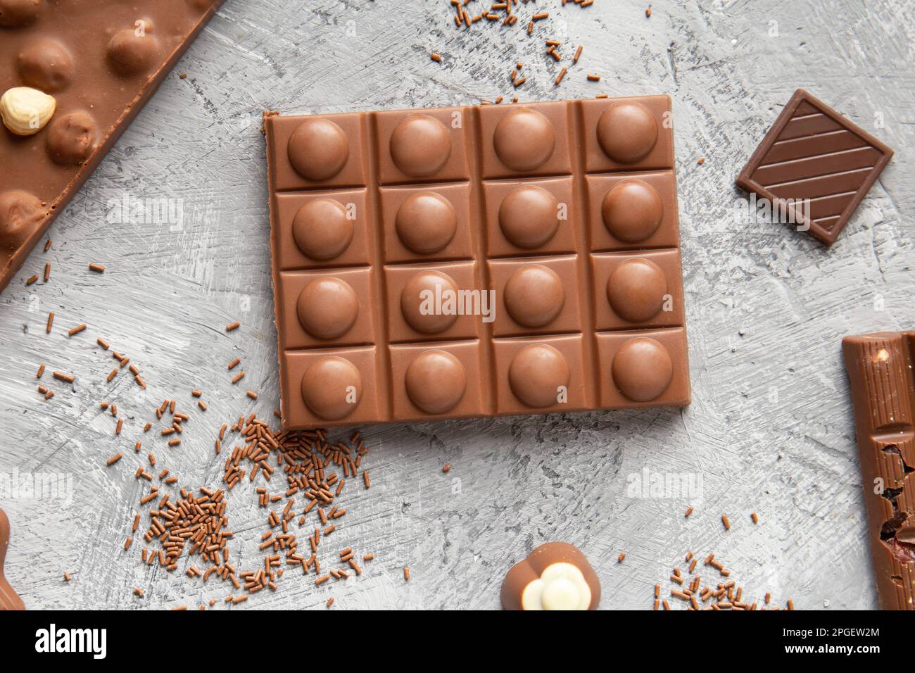 Barrette di cioccolato al latte di diverse dimensioni, dolci, patatine di cioccolato su sfondo grigio vista dall'alto. Cioccolato fatto a mano con nocciole primo piano. Foto Stock