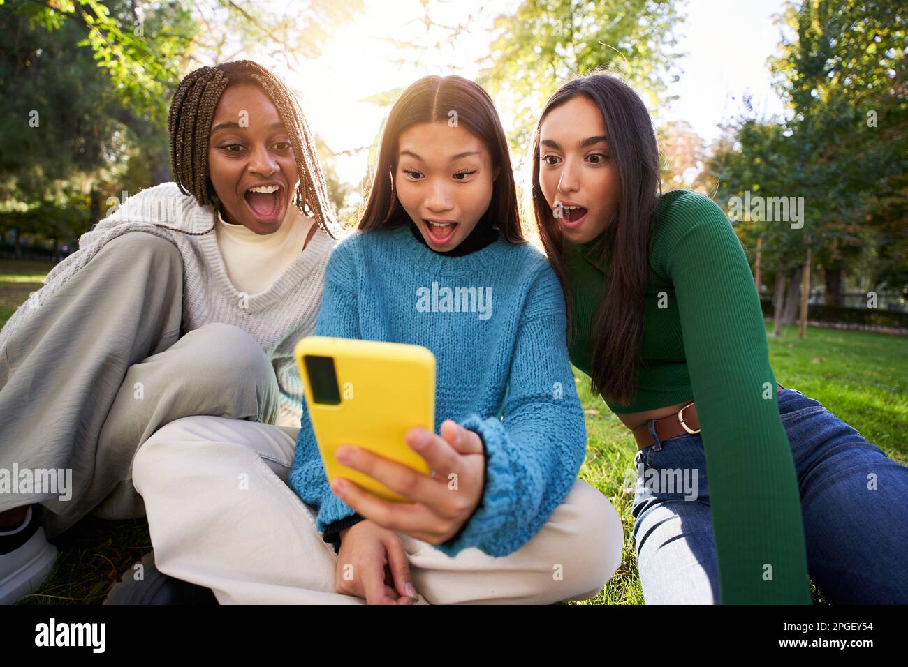 Le persone che guardano lo schermo del cellulare affascinato con la bocca aperta. Tre giovani donne che usano una cellula. Foto Stock