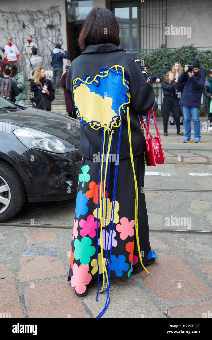MILANO, ITALIA - 24 FEBBRAIO 2023: Donna con cappotto nero con cuore giallo e blu con archi prima della sfilata Sportmax, sfilata della Fashion Week di Milano Foto Stock