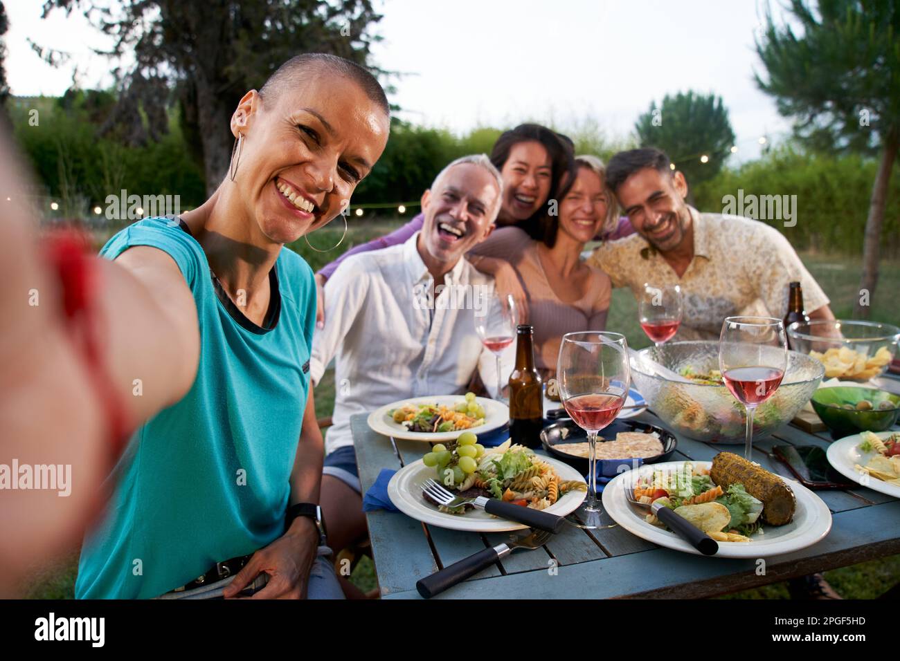 Gruppo di amici che prendono selfie all'ora di cena barbecue. Persone di mezza età che si raffreddano fuori mangiare e bere sulla terrazza casa patio. Cibo e. Foto Stock