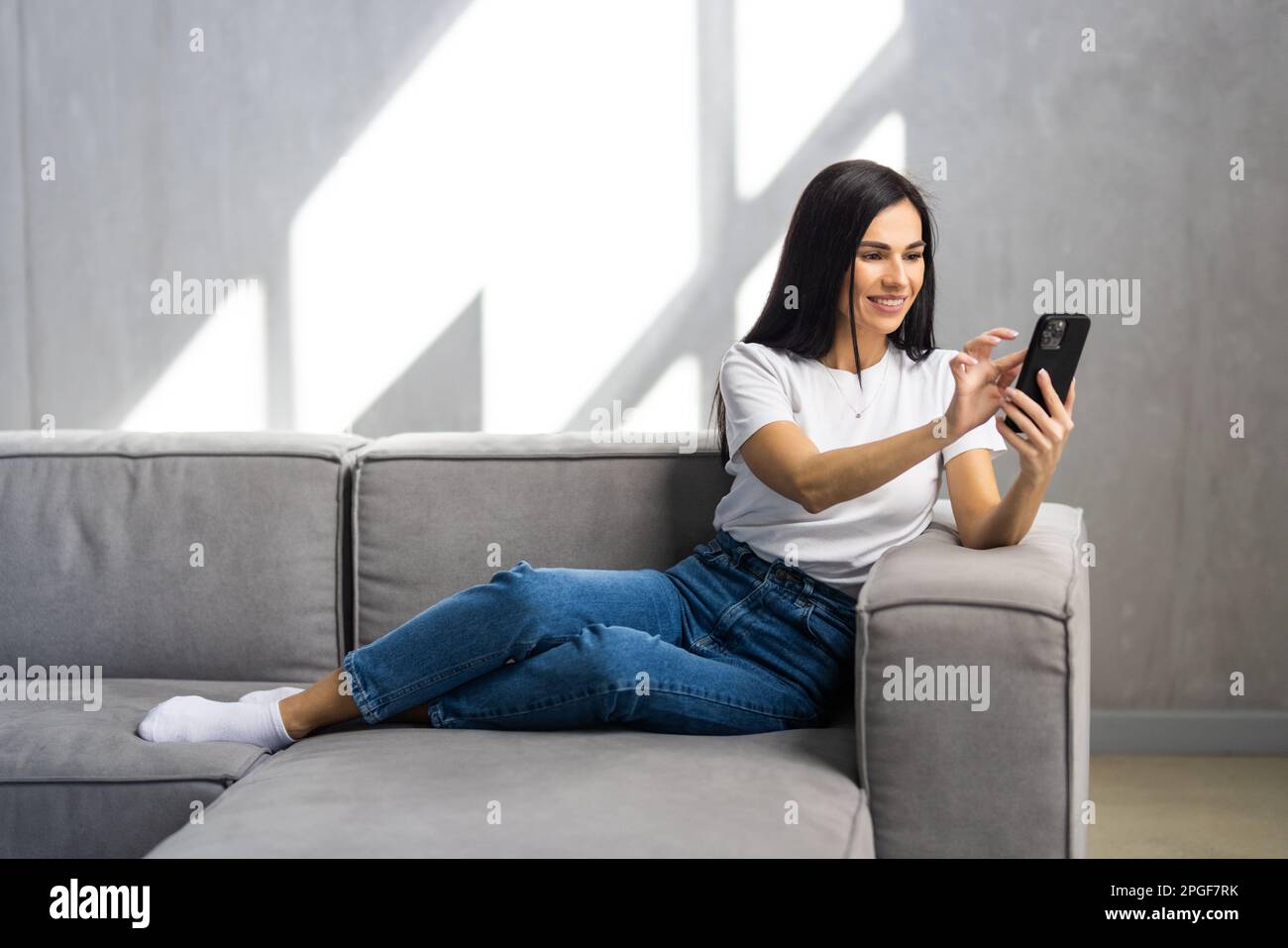 Calma donna attraente sedersi sul divano utilizzando smartphone, primo piano. Generazione e tecnologia moderna uso quotidiano per divertimento, fare ordine a distanza, comunicazione r Foto Stock