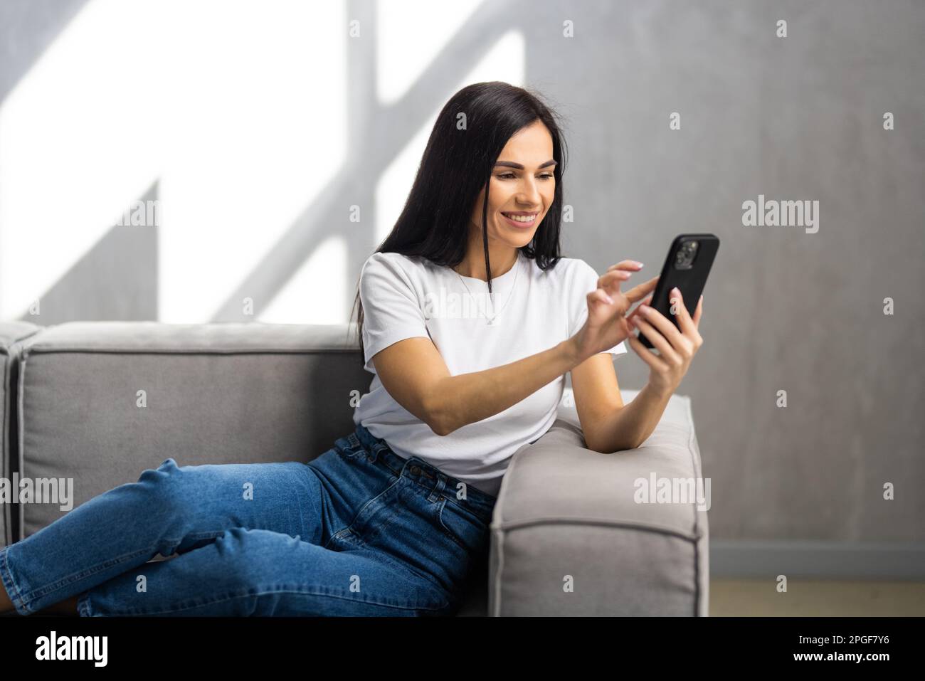 Calma donna attraente sedersi sul divano utilizzando smartphone, primo piano. Generazione e tecnologia moderna uso quotidiano per divertimento, fare ordine a distanza, comunicazione r Foto Stock