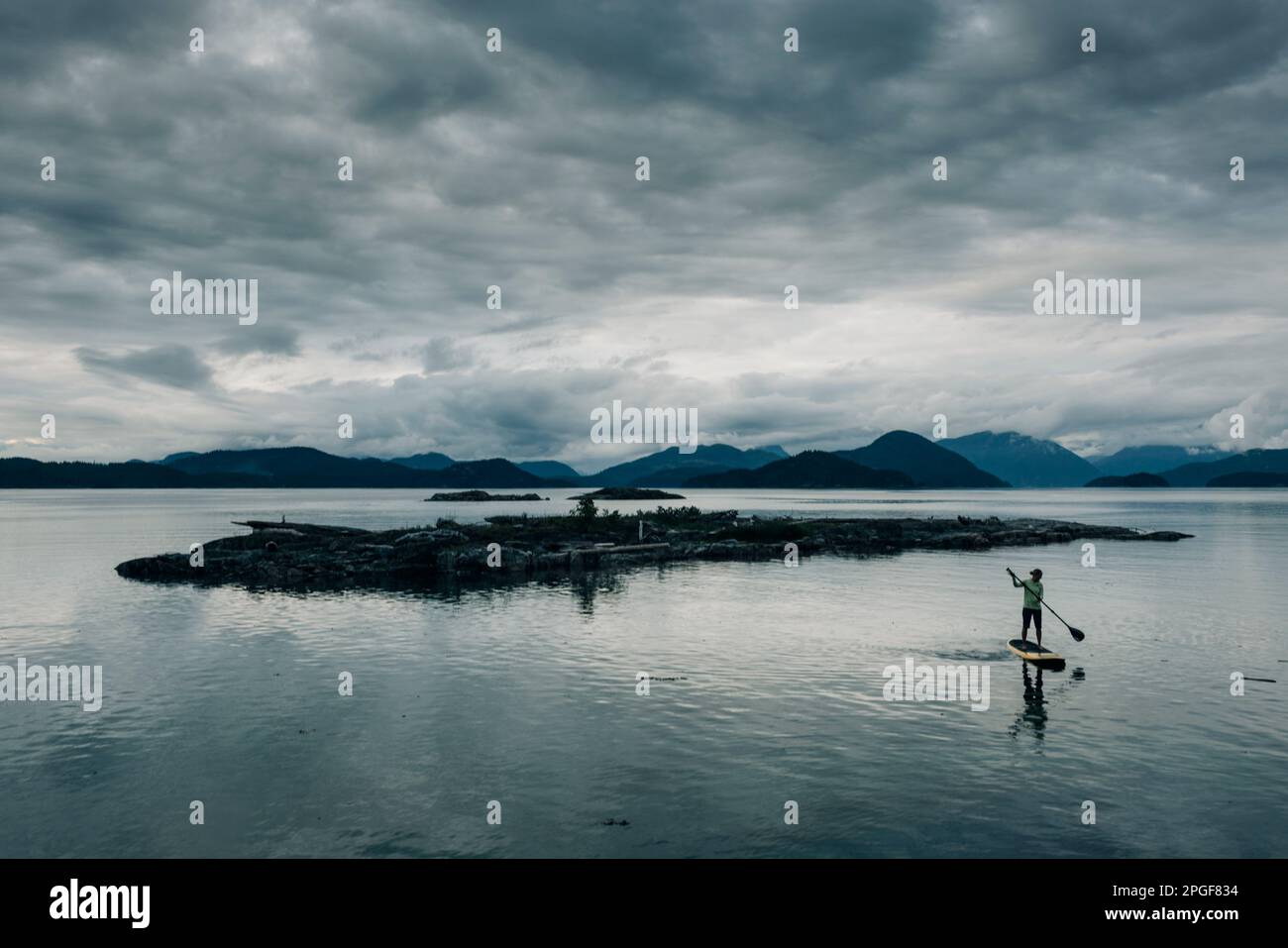 Una donna pagaia sulla sua tavola di pagaia standup al crepuscolo. Foto Stock