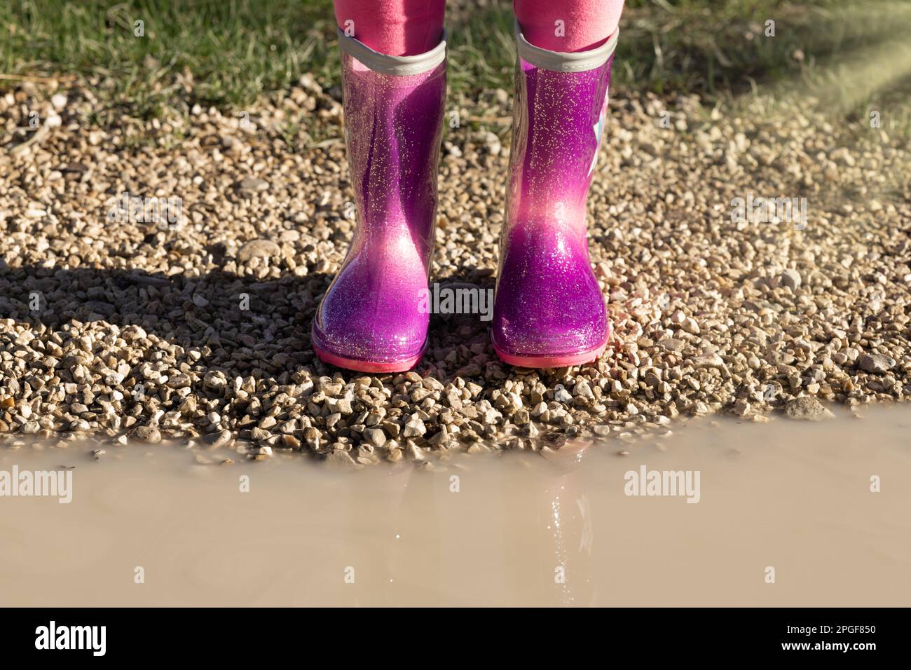 Bambino che indossa nuovi stivali di gomma da pioggia rosa brillante in piedi vicino a pozza fangosa, senza volto. Prescolare in wellies. Calzature per il tempo piovoso Foto Stock