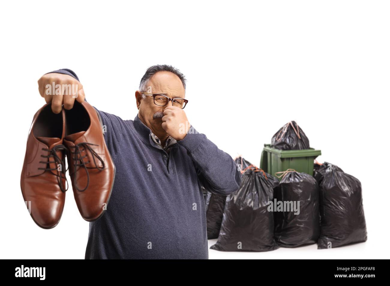 Uomo maturo che tiene un paio di scarpe stinky vicino a un bidone della spazzatura isolato su sfondo bianco Foto Stock