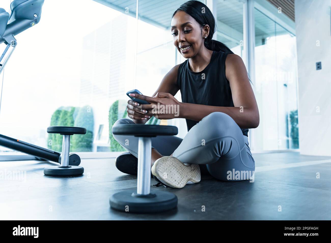 Una donna afroamericana seduta in palestra - usando il suo telefono Foto Stock