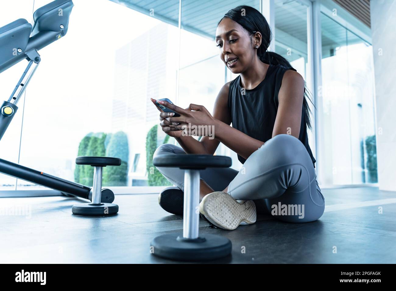 Una donna afroamericana seduta in palestra - usando il suo telefono Foto Stock