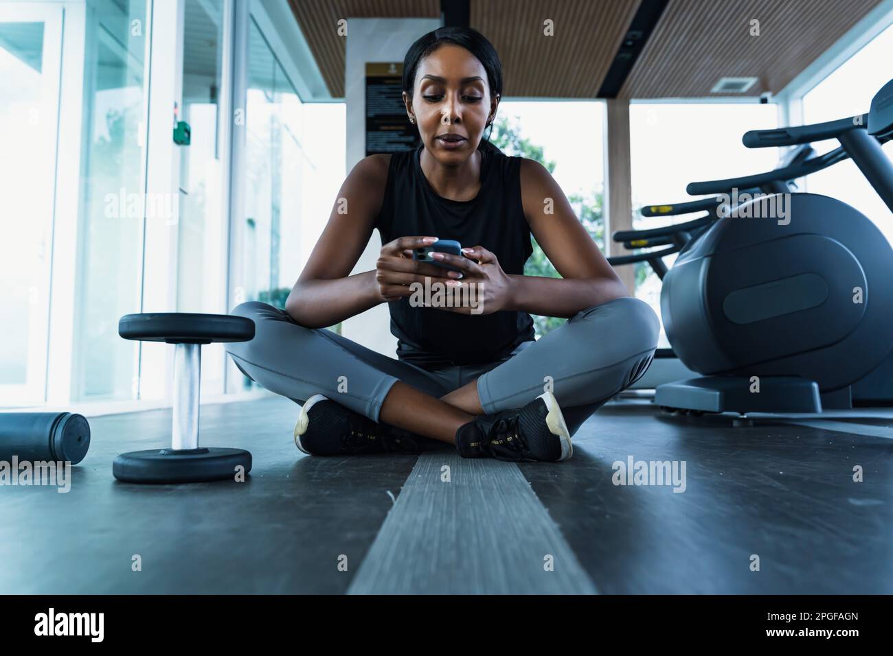 Una donna afroamericana seduta in palestra - usando il suo telefono Foto Stock