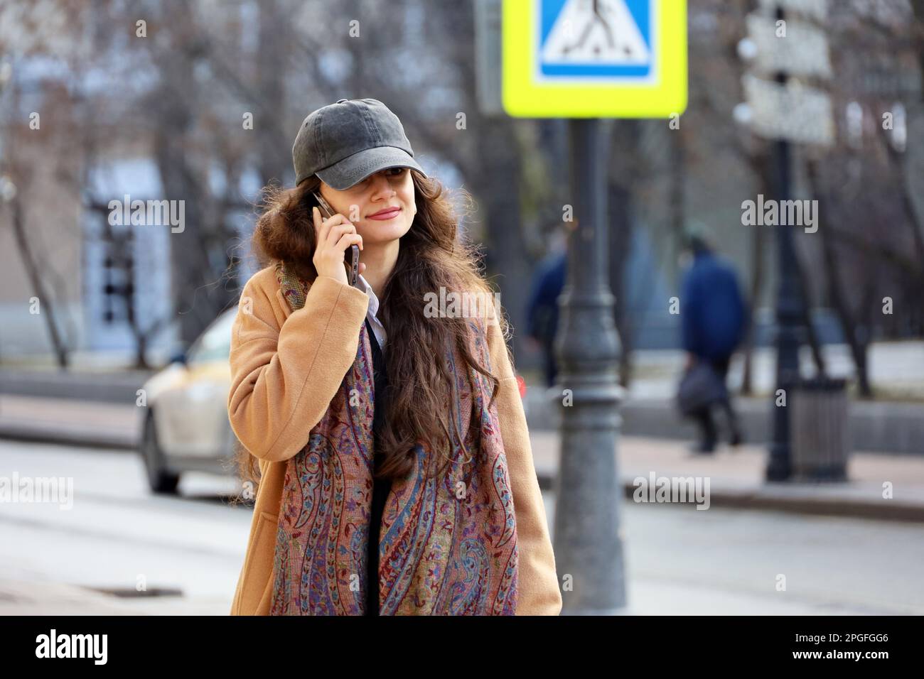 Donna in cappellino da baseball che parla sul telefono cellulare mentre cammina per strada. Utilizzo dello smartphone nella città primaverile Foto Stock