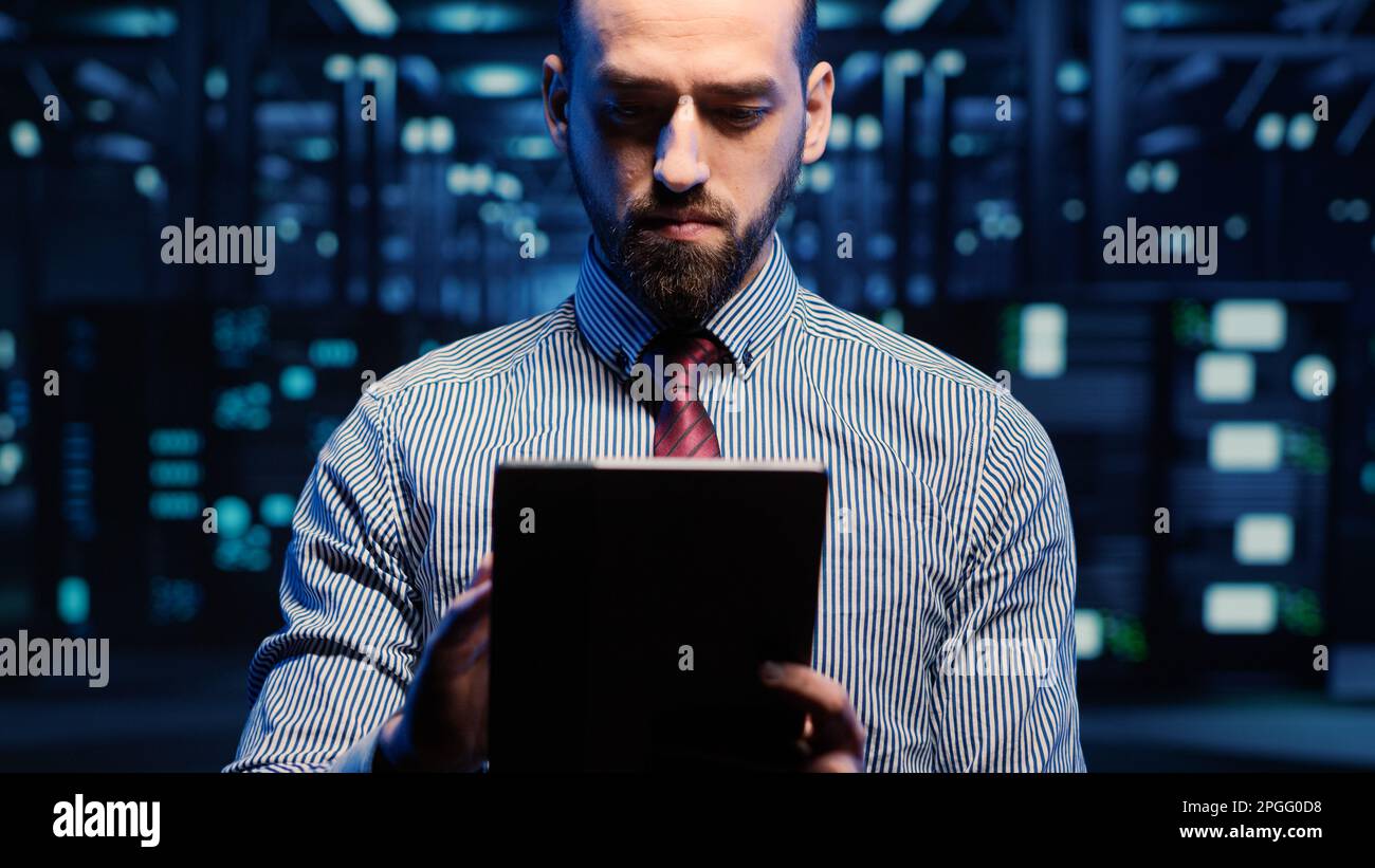 Tecnico INFORMATICO che lavora nel data center con tablet, guardando gli armadi dei rack nella sala server digitale. Ingegnere professionista che attiva il sistema di archiviazione hardware. Scatto manuale. Foto Stock