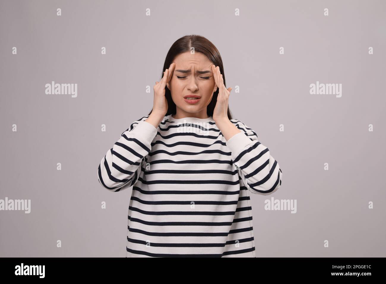 Donna che soffre di mal di testa su sfondo grigio chiaro. Sintomi del freddo Foto Stock