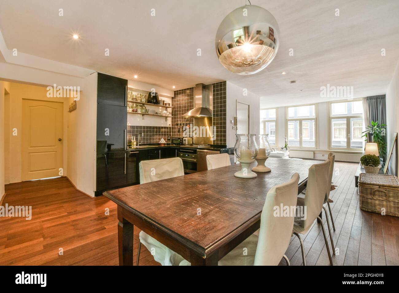 una cucina e zona pranzo in una casa con pavimenti in legno duro, pareti bianche, pavimento in legno e elettrodomestici neri Foto Stock