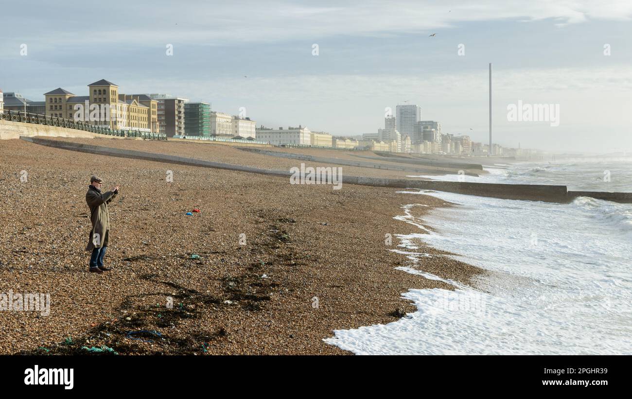 Immagine a colori di un uomo sulla spiaggia di Brighton in un cappotto e cappello piatto Foto Stock