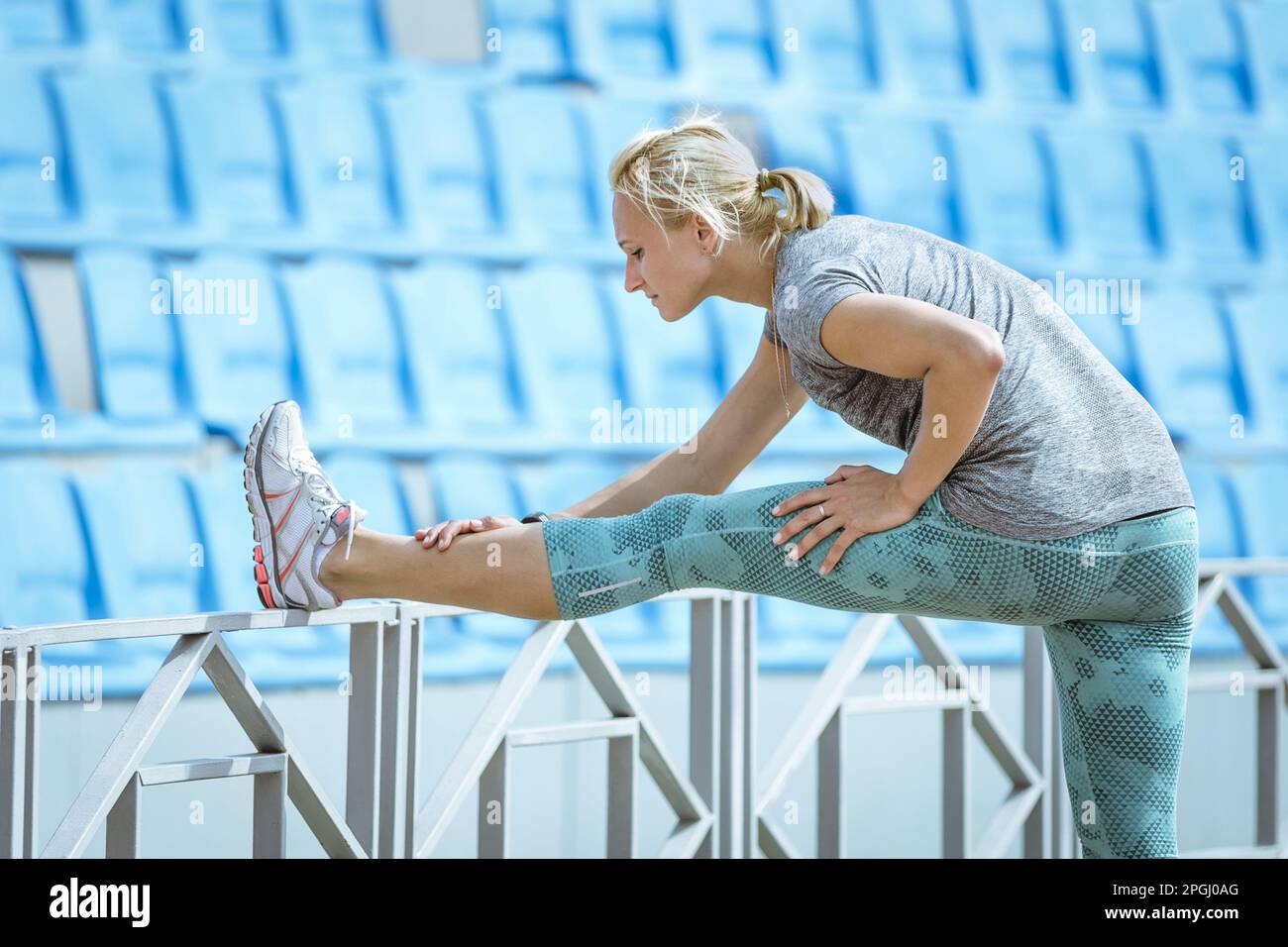 runner femminile che fa esercizio di stretching, si inclina in avanti alla gamba, si scalda prima dell'allenamento di atletica Foto Stock