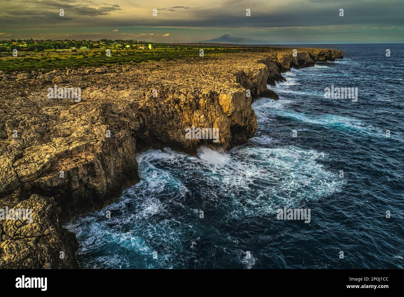 Le scogliere sulle quali si infrangono le onde tempestose del mare lungo la costa della Riserva Naturale del Plemmirio. Sullo sfondo, il vulcano Etna. Sicilia Foto Stock