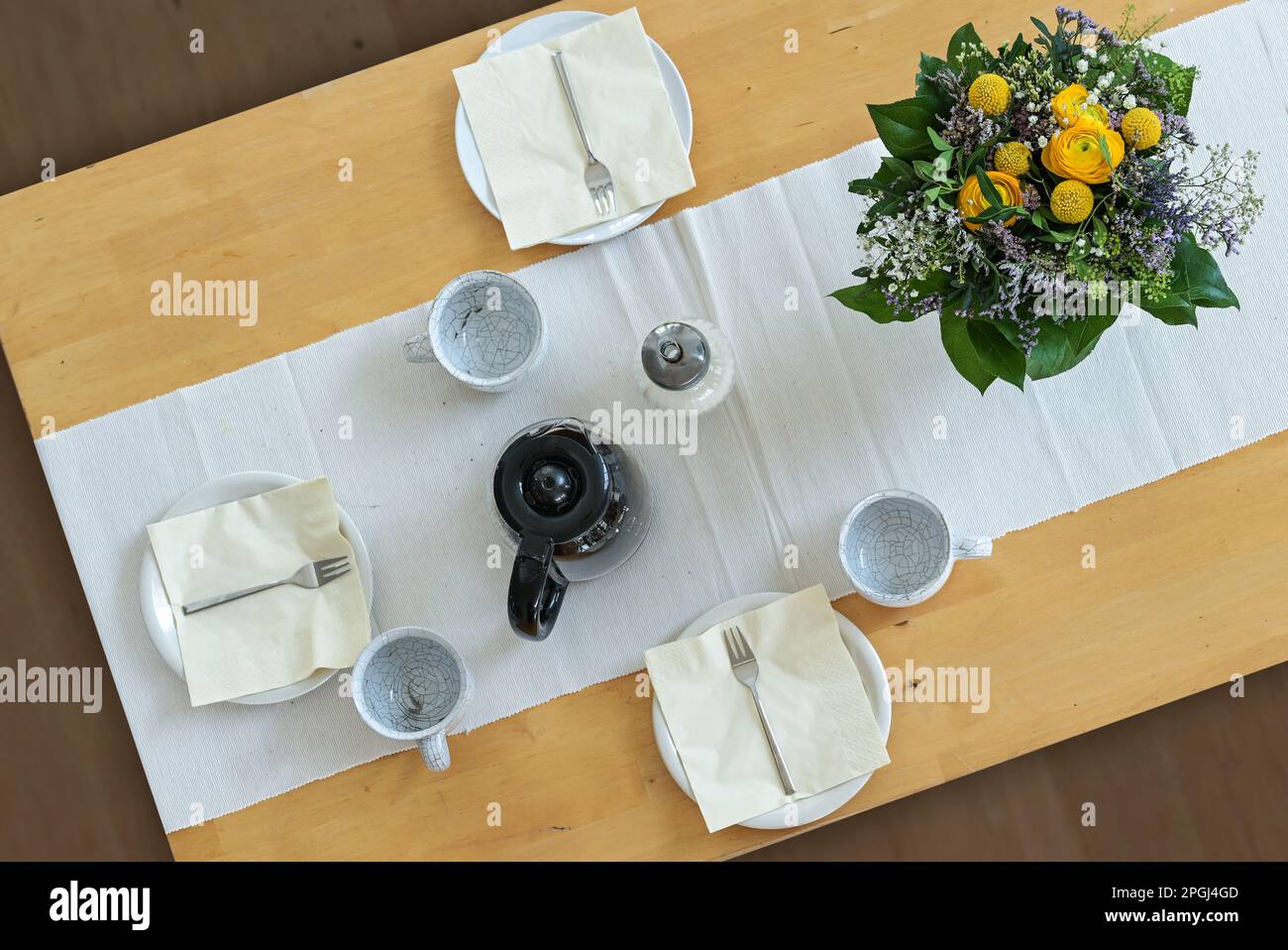 Tavolo in legno con tre piatti, tazze, tovaglioli, caffettiera e un bouquet di fiori su un cannello da tavolo bianco, vista dall'alto ad angolo, focus selezionato Foto Stock