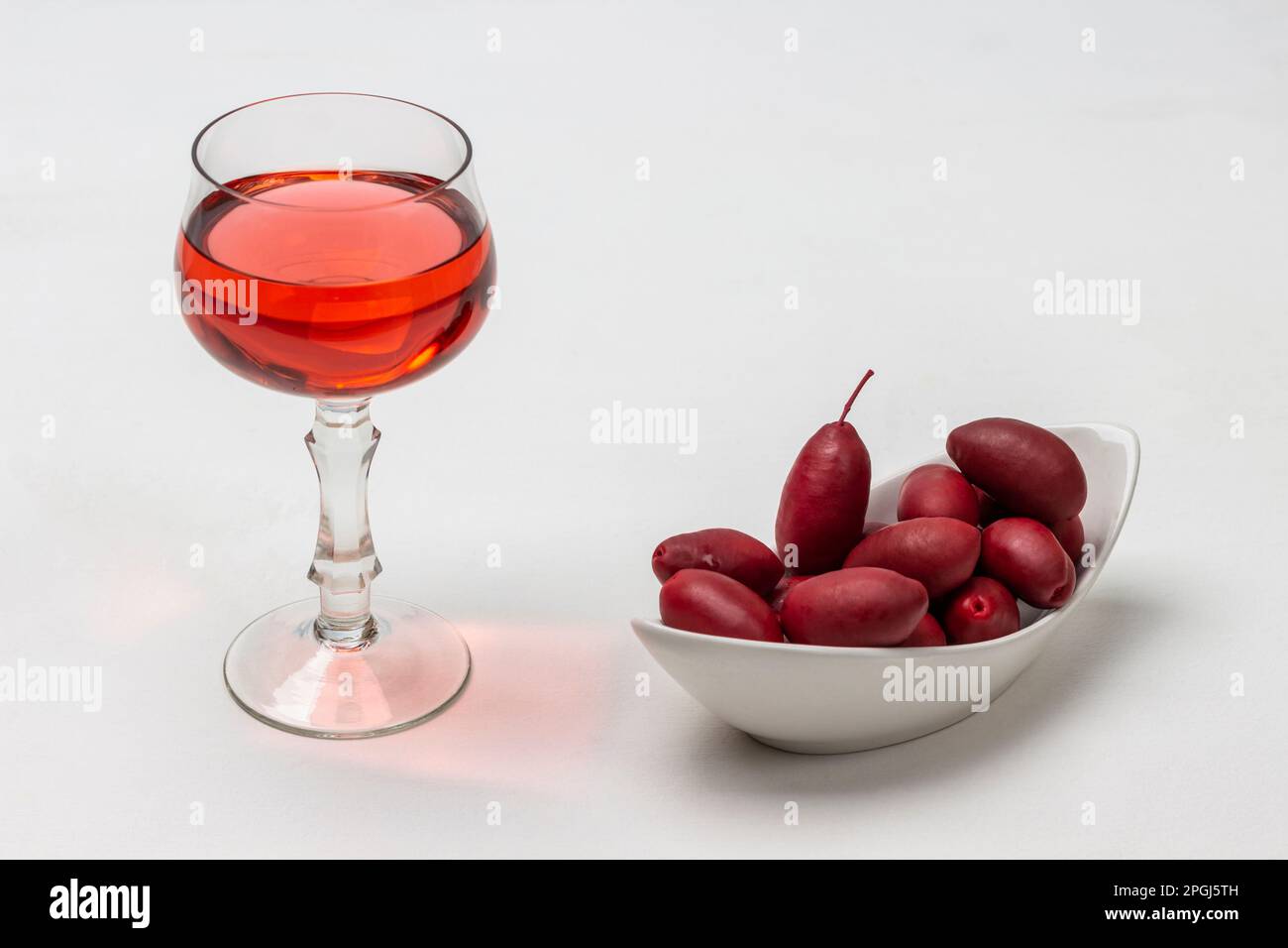 Bicchiere con vino rosso. Olive di Borgogna in una ciotola bianca. Sfondo bianco. Foto Stock