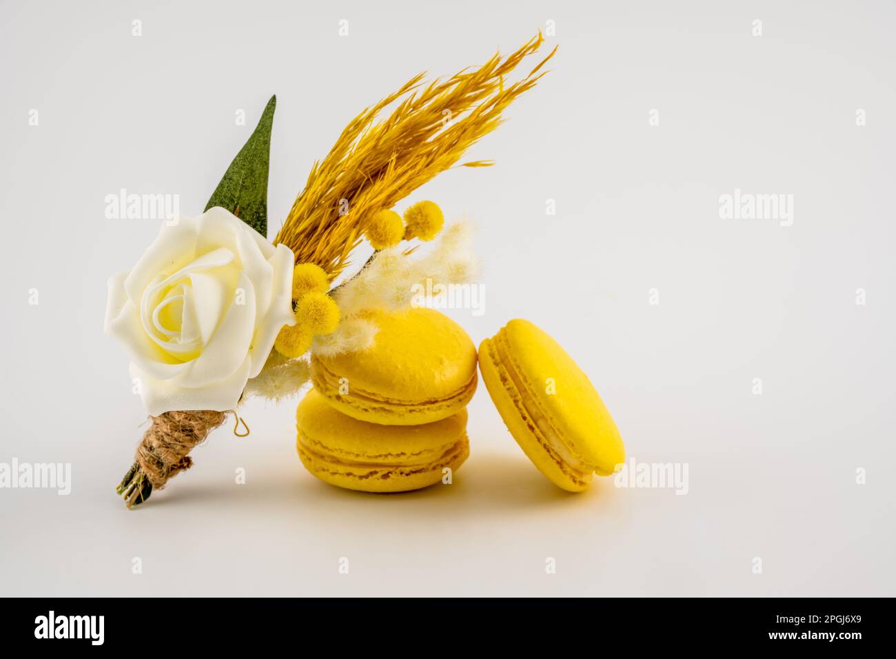 bottone floreale di nozze buco appoggiato contro una pila di macaron gialli isolato su uno sfondo bianco Foto Stock