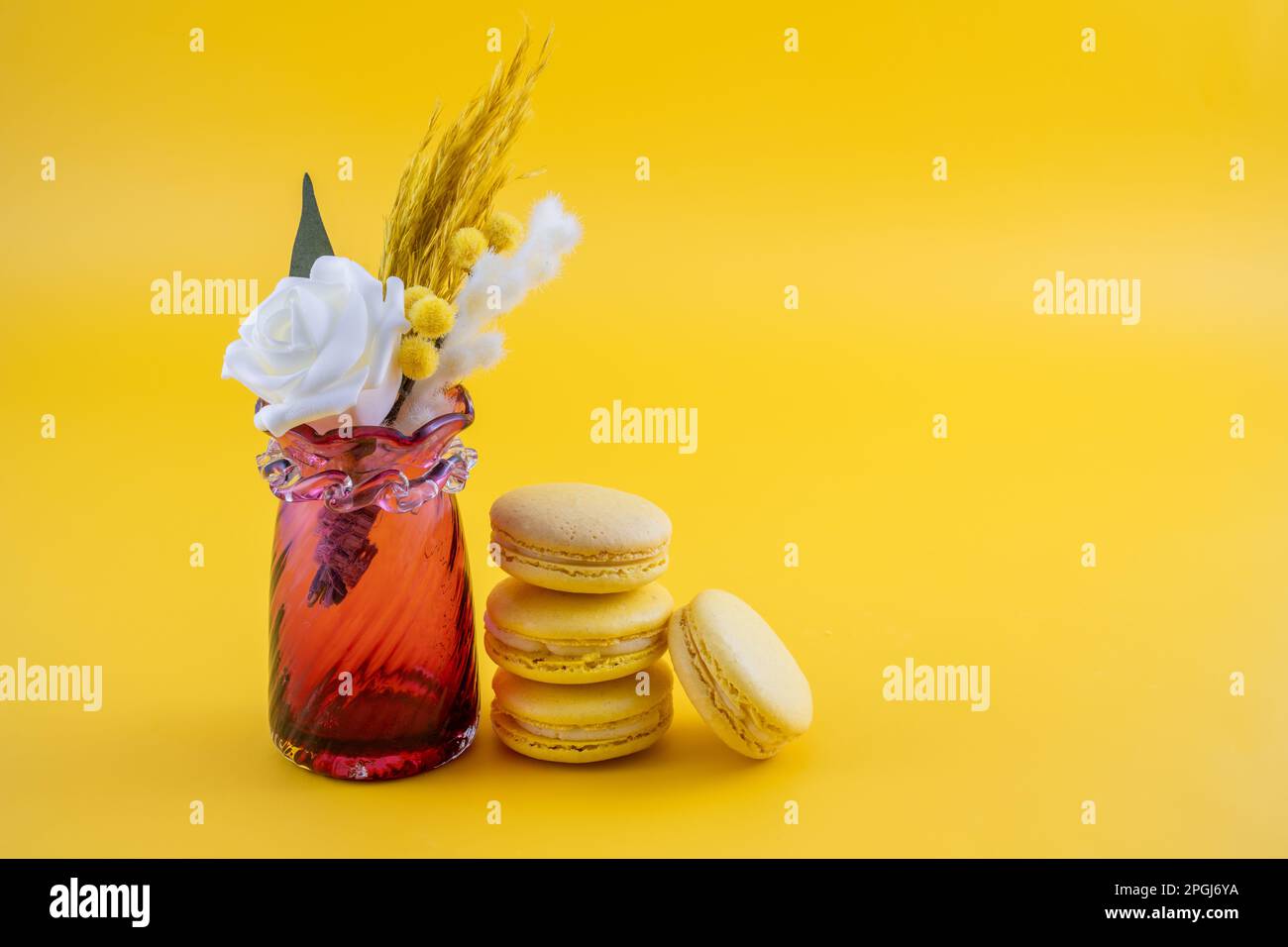 vaso rosso con arrangiamento floreale con macaroon su fondo giallo Foto Stock