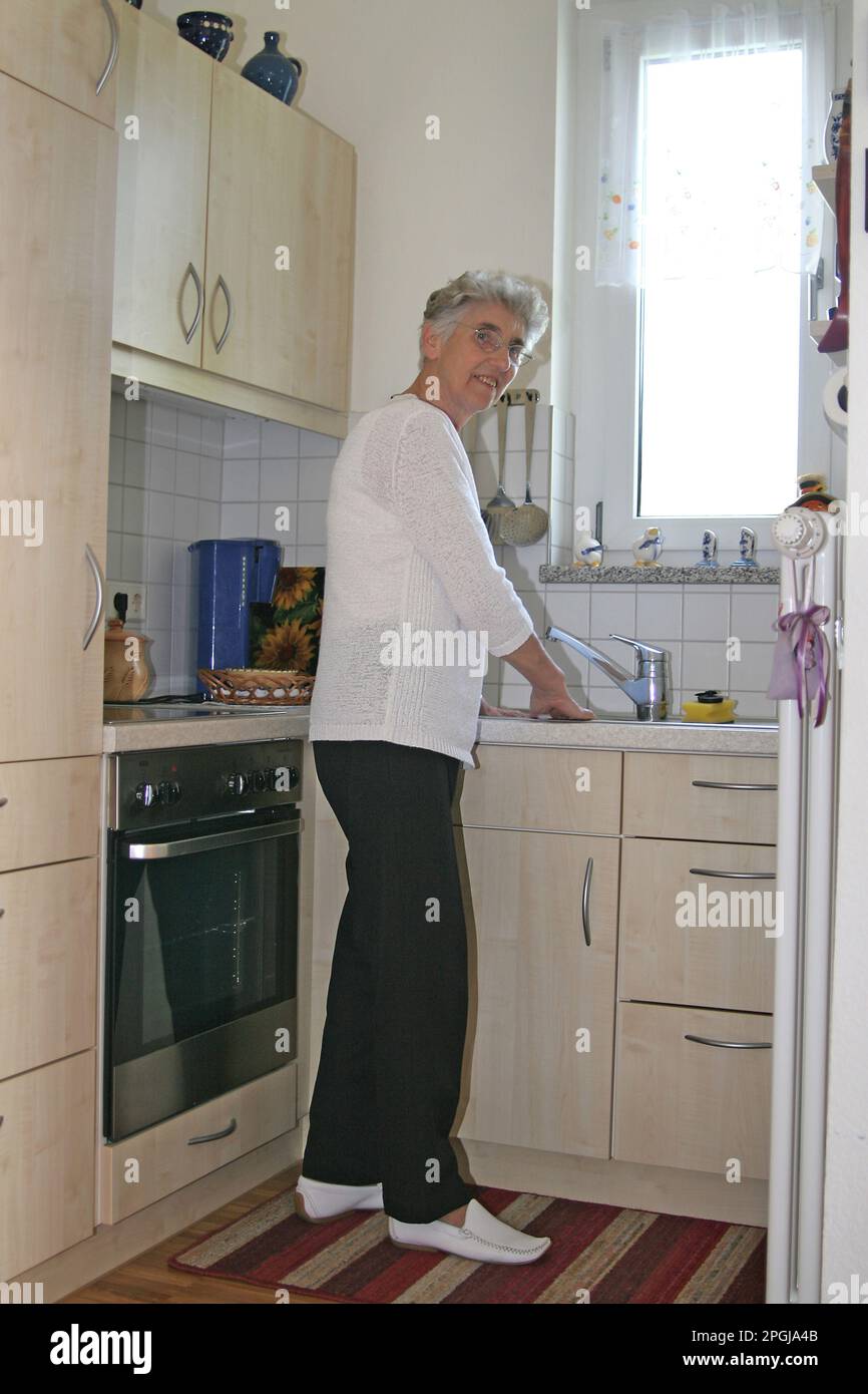 donna anziana in piedi al lavello della cucina nella sua piccola cucina Foto Stock