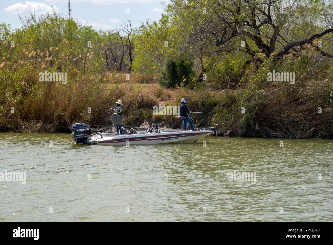 Due persone pescano dalla loro piccola barca sul fiume Rio Grande, vicino alla riva densamente vegetata del fiume sul lato degli Stati Uniti. Foto Stock