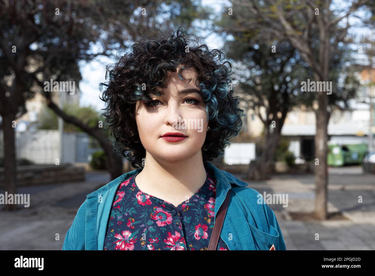 Ritratto di una ragazza brunetta sorridente di venticinque anni vestita con un abito vintage blu con un motivo e una blusa verde con una borsa piccola Foto Stock