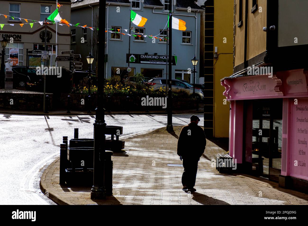 L'uomo cammina per strada in Ardara, Contea di Donegal, Irlanda. Bandiera della Repubblica Nazionale che vola per la Giornata di San Patrizio. Foto Stock