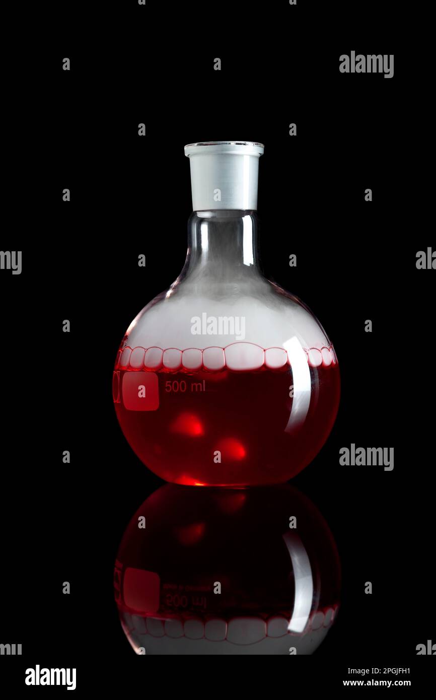 Una beuta chimica a fondo piatto in vetro con fluido rosso e fondo nero isolato dal fumo Foto Stock