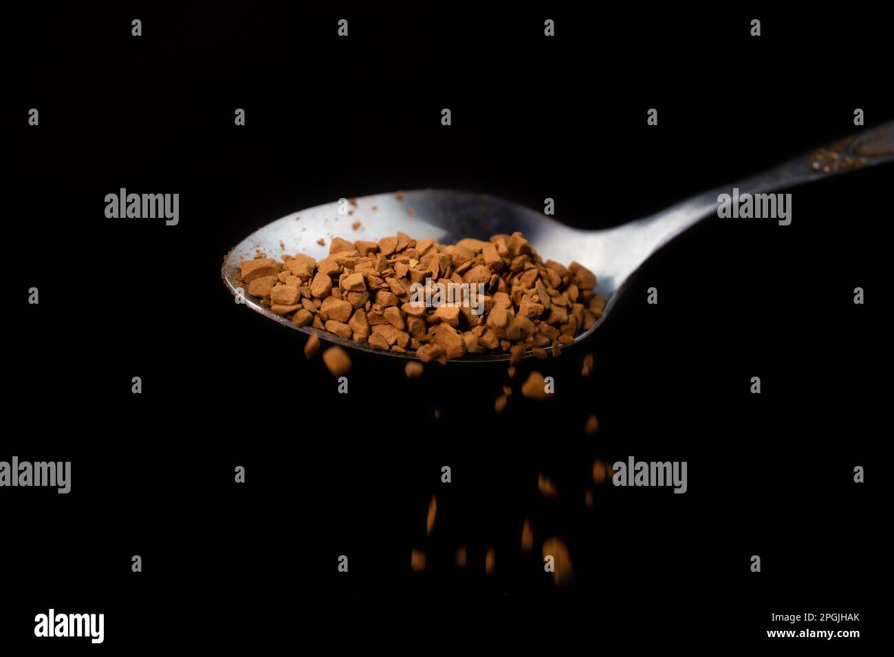 Primo piano del caffè granulare che fuoriesce da un cucchiaino da tè su sfondo nero, fotografia macro Foto Stock