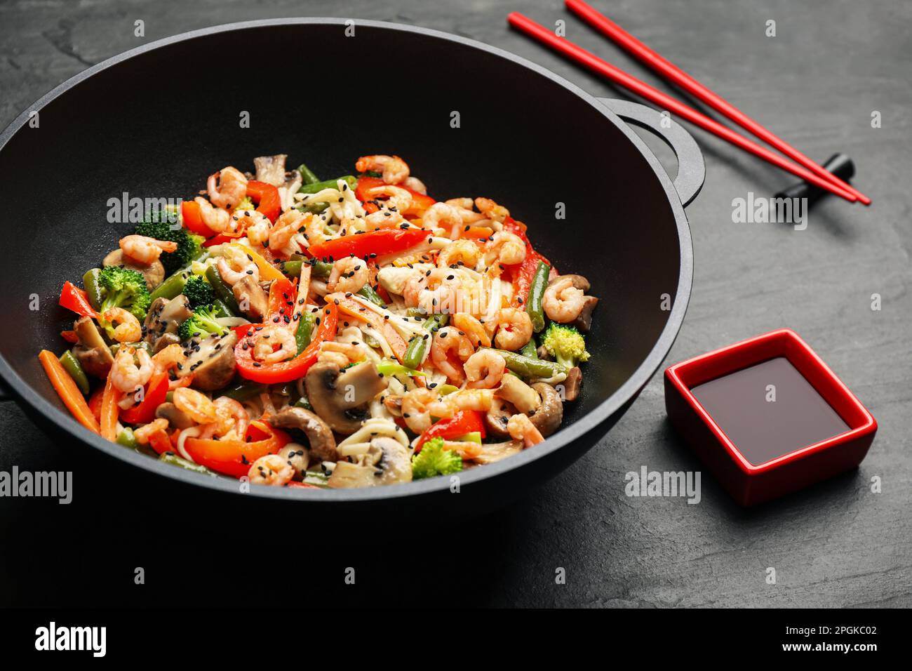 Mescolare le tagliatelle fritte con funghi, gamberetti e verdure in wok sul tavolo nero, primo piano Foto Stock