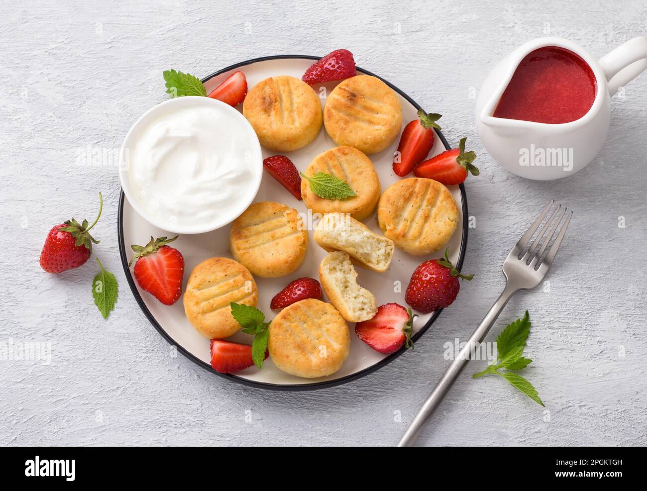 Gnocchi di formaggio casereccio cotti in casa con salsa di fragole, fragole fresche e panna acida, decorata con menta su sfondo grigio chiaro, top vi Foto Stock