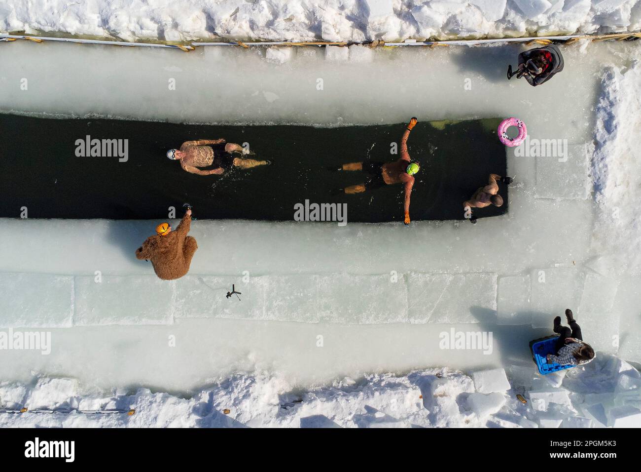 Tre persone nuotano nell'acqua fredda di un lago ghiacciato in modo divertente a sud di Quebec City il 5 marzo 2023. Foto Stock