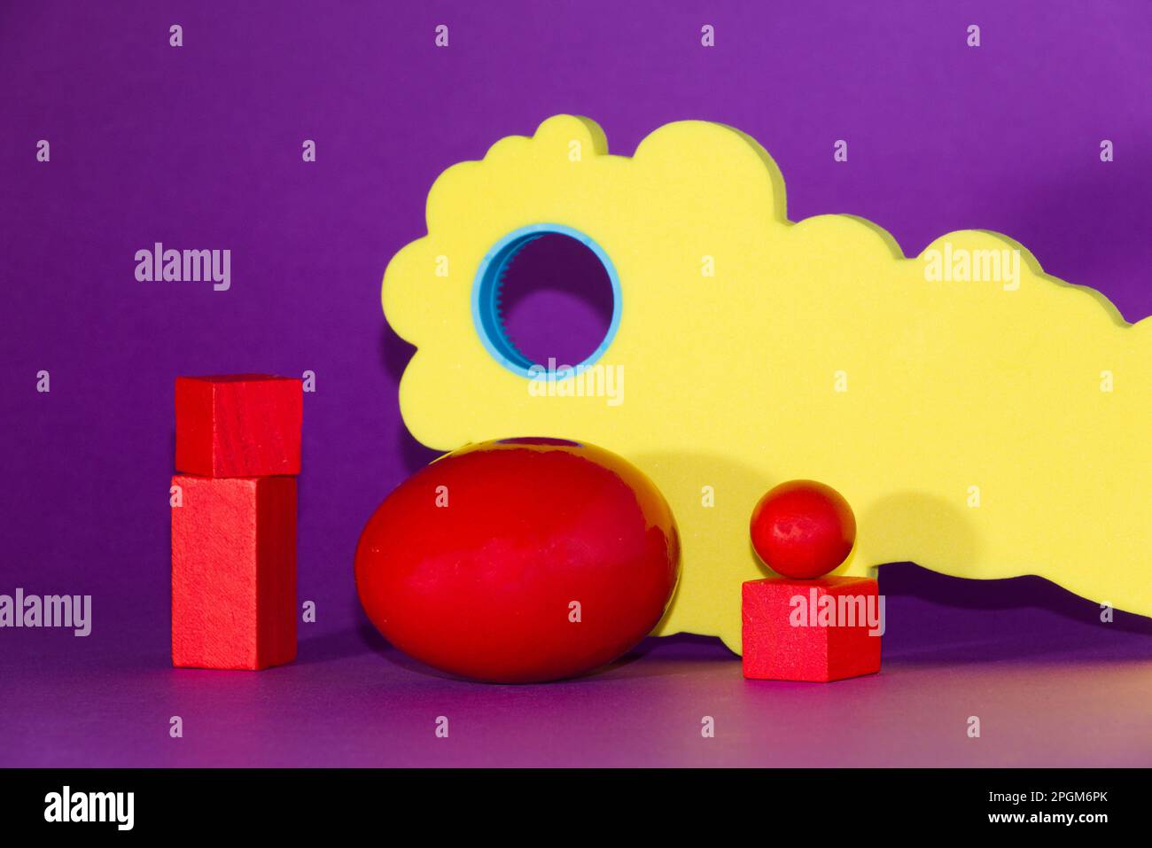 Uovo di Pasqua rosso su sfondo viola, varie forme geometriche intorno a quello Foto Stock