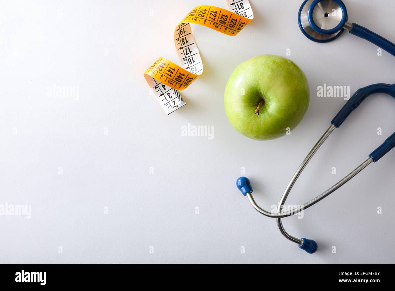 Apple, stetoscopio e metro a nastro su un tavolo bianco che rappresenta la salute, la nutrizione e il controllo del corpo. Vista dall'alto. Foto Stock