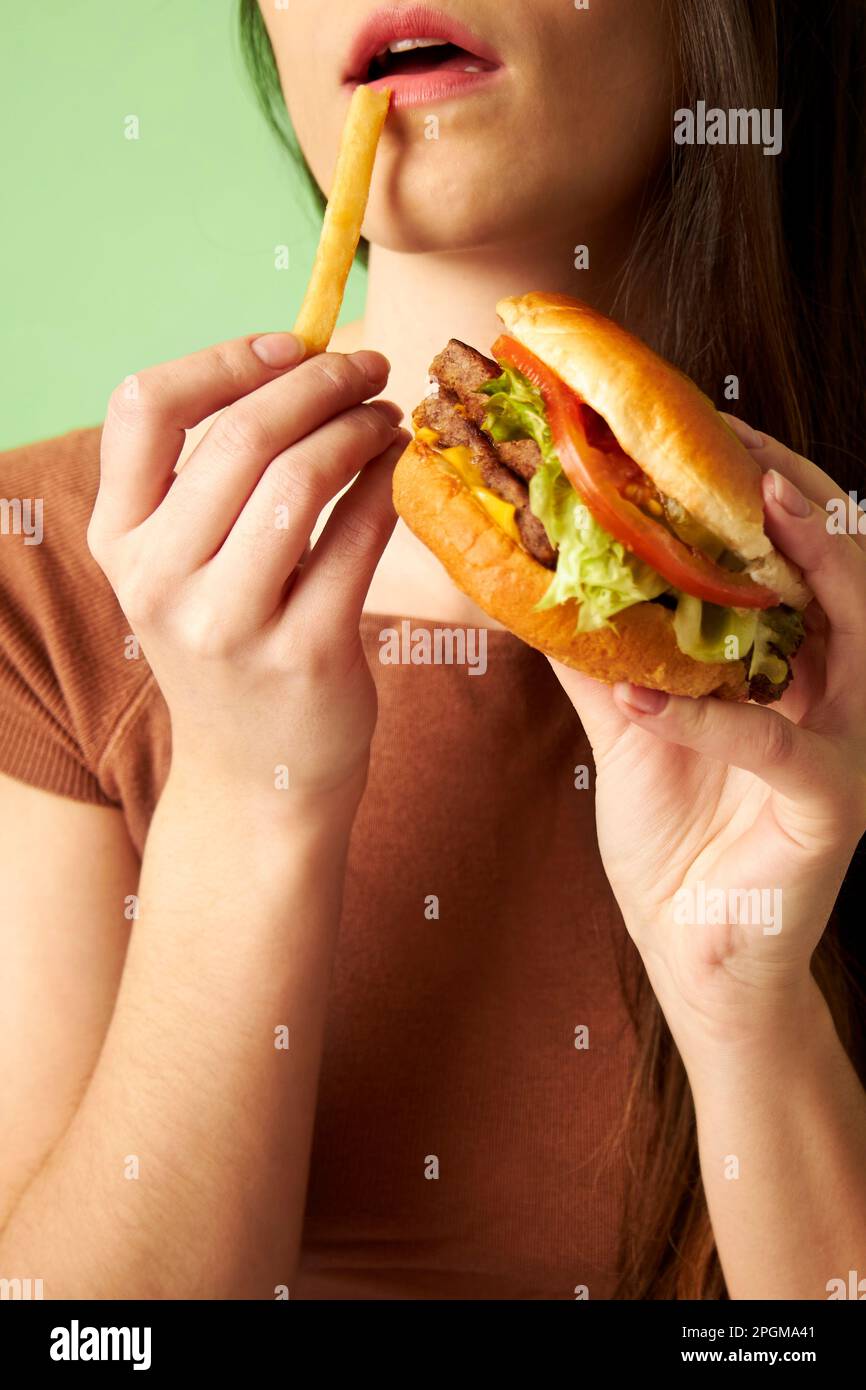 Donna che tiene un fritto francese e hamburger cheeseburger fino a bocca mangiare Foto Stock