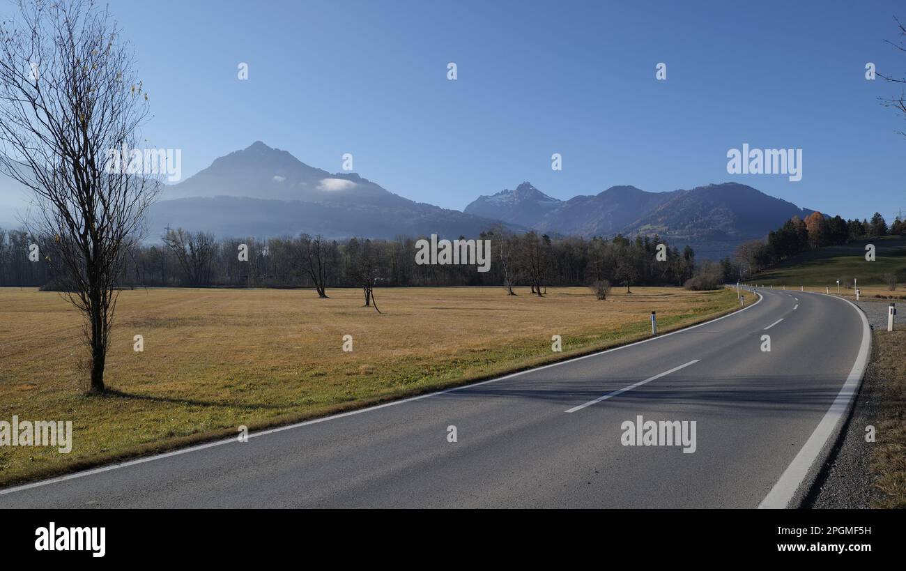 Autostrada al sole con curva con grande campo arido, alberi senza foglie, nebbia e montagne sullo sfondo Foto Stock