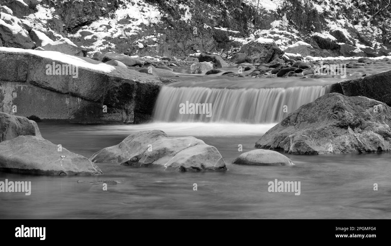 Piccola cascata da un ruscello in inverno con grandi pietre in acqua in bianco e nero Foto Stock