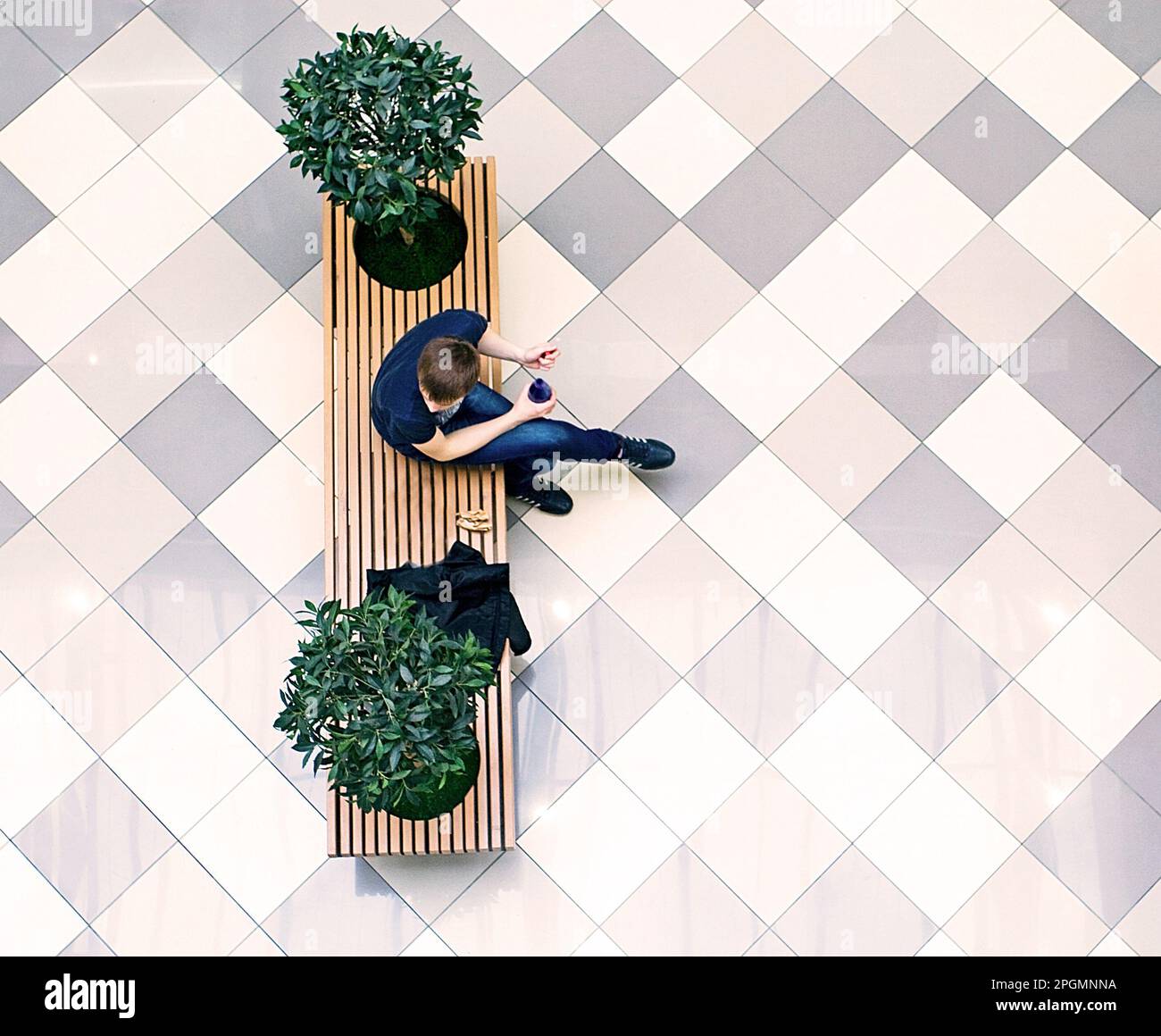 giovane uomo che morde seduto sulle panchine, una vista dall'alto dal supermercato Foto Stock