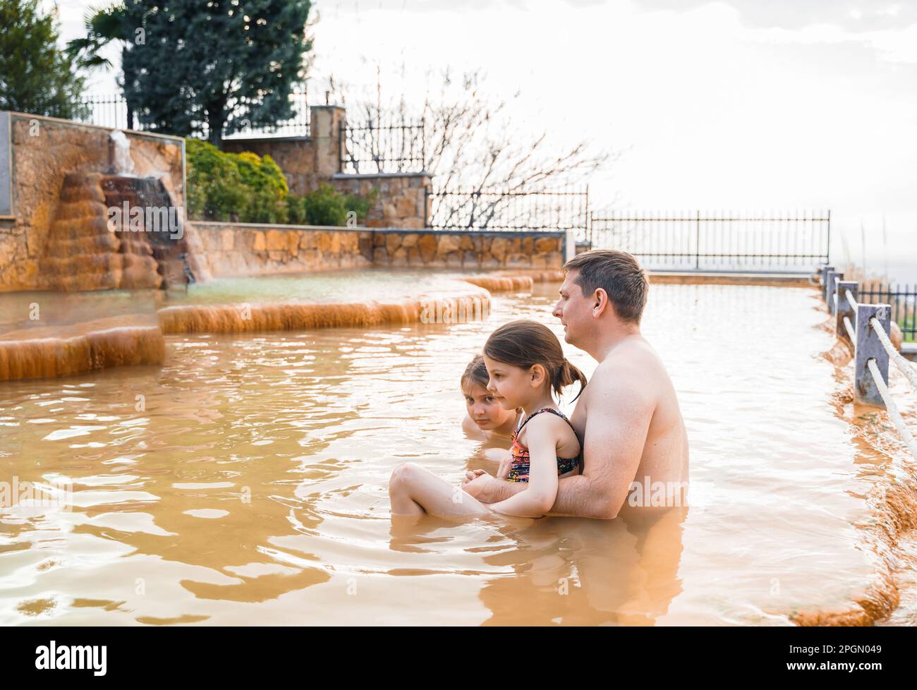 Famiglia, papà e bambini fanno il bagno, nuotano nelle sporche sorgenti termali all'aperto. Piscina con acqua termale e fanghi naturali, argillosi e verdi gialli. Spa wellnes Foto Stock