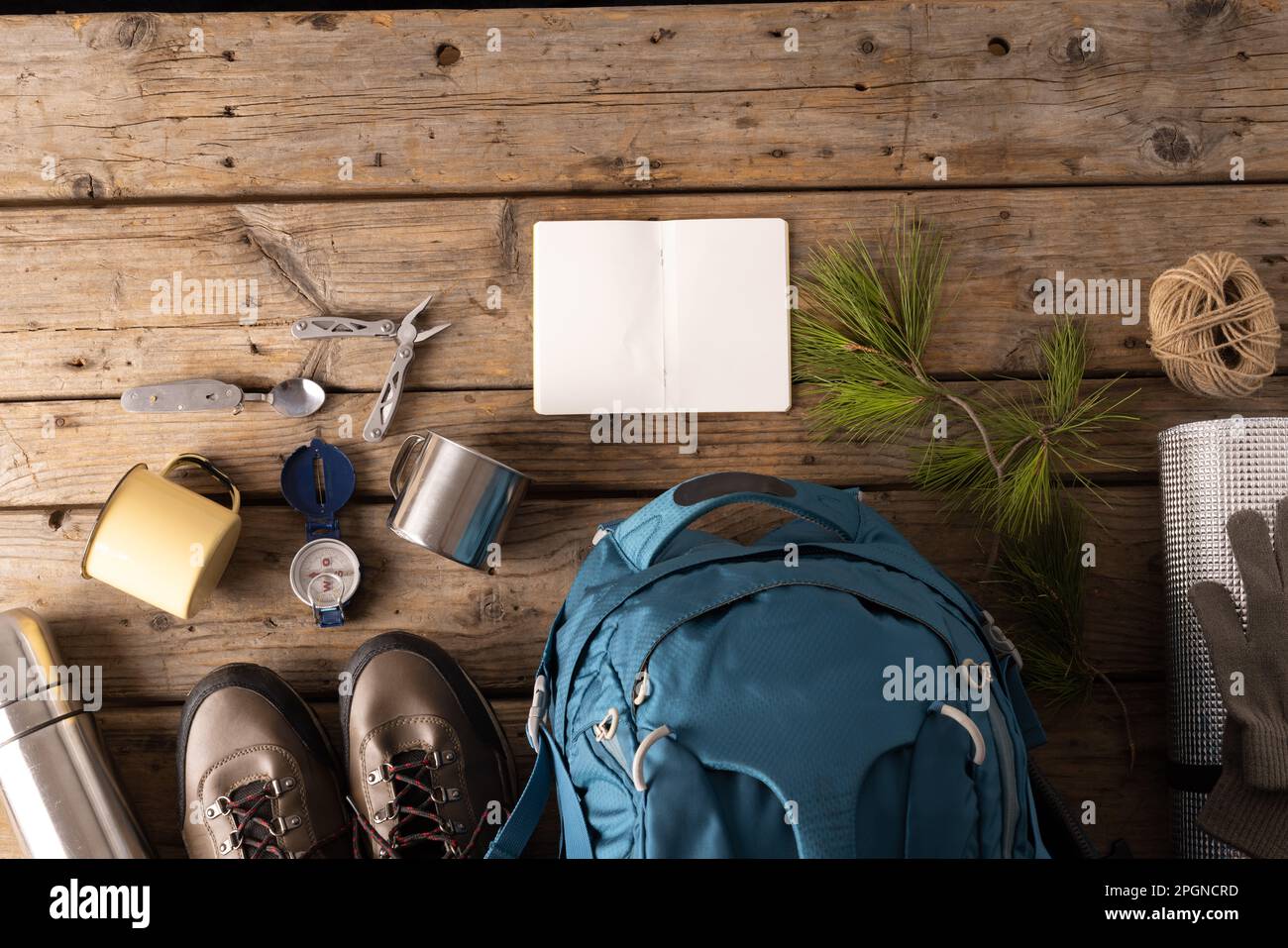 Attrezzatura da campeggio di zaino, tazza di metallo e taccuino vuoto su sfondo di legno con spazio copia Foto Stock