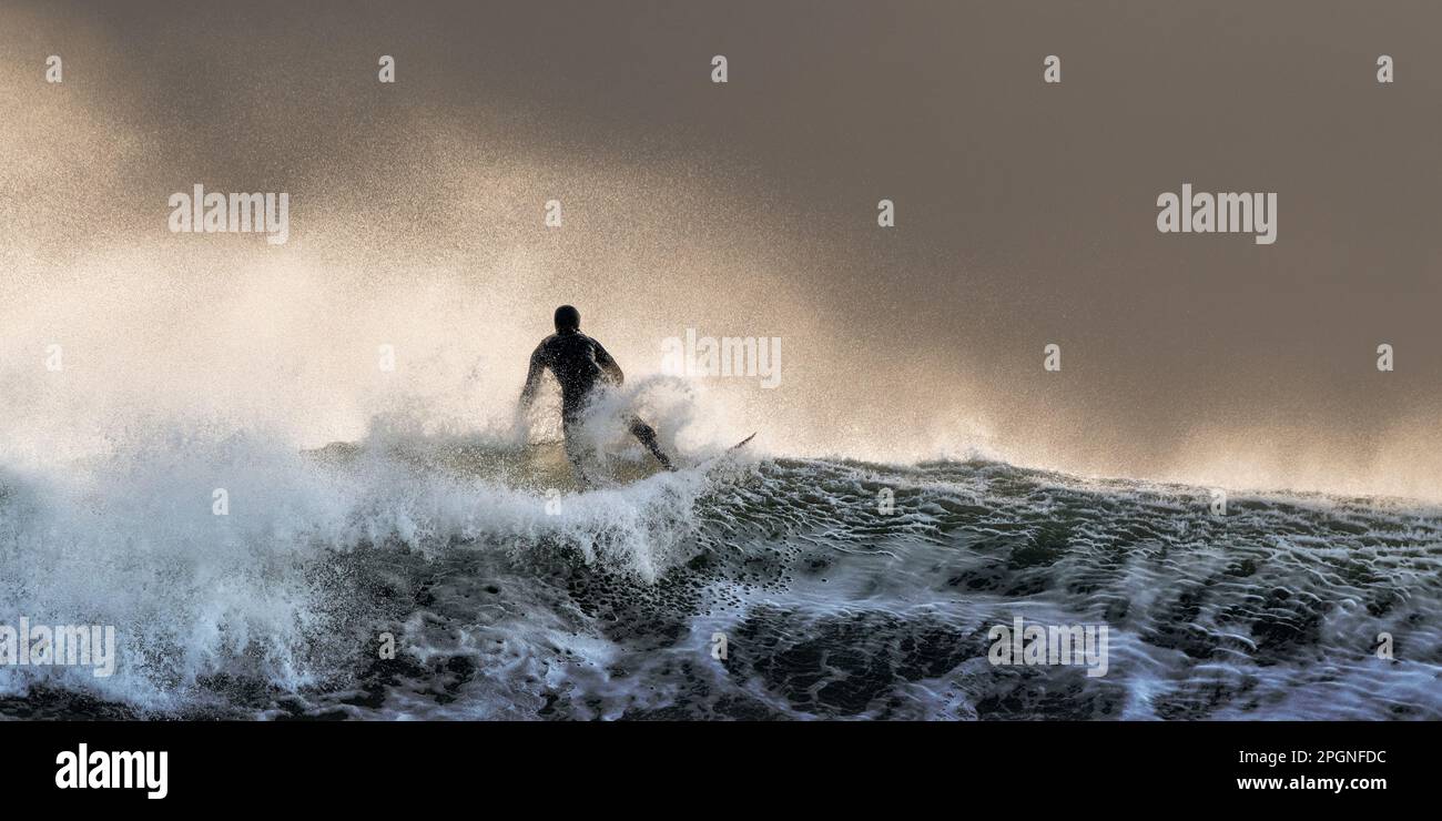 Surf spensierato sul mare ondulato al tramonto Foto Stock