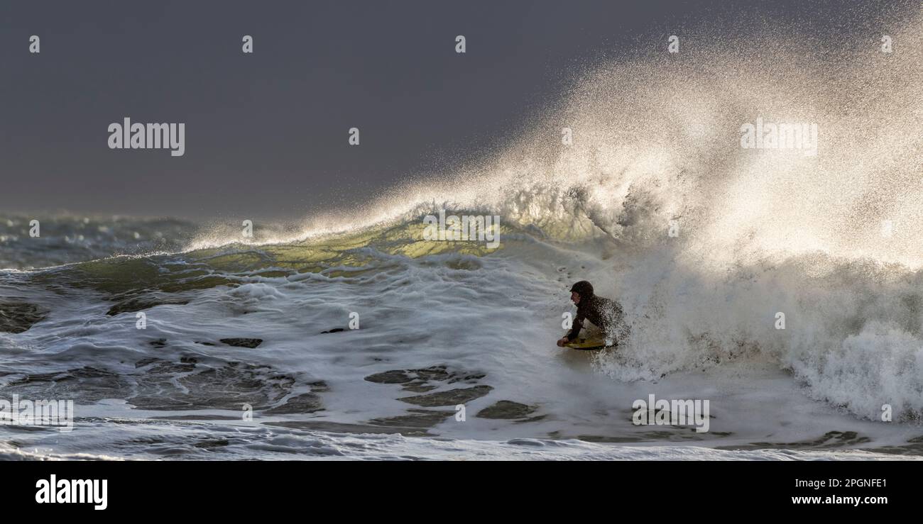 Giovane uomo che nuota con tavola da surf in mare ondulato in vacanza Foto Stock