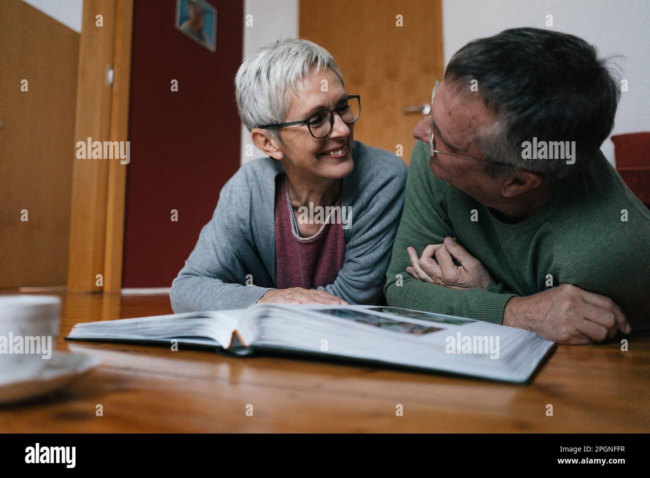 Felice coppia senior sdraiato sul pavimento a casa con album di foto Foto Stock