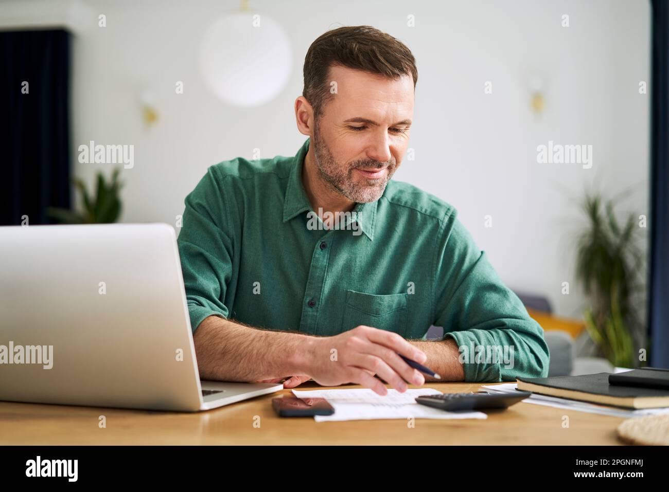 Uomo a casa seduto con notebook e documenti che esaminano le finanze domestiche Foto Stock