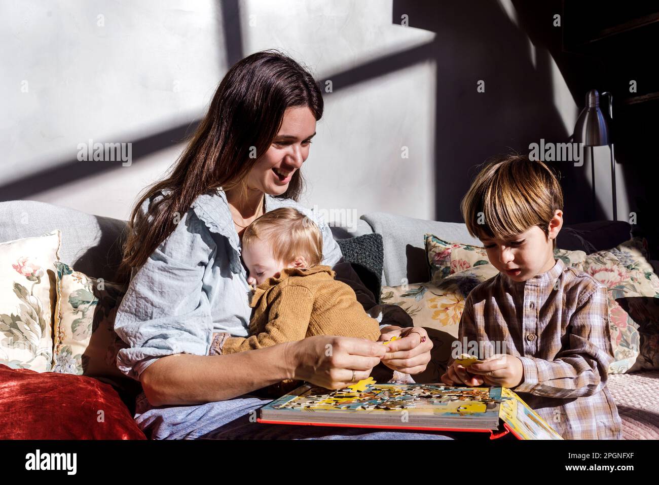 Madre sorridente che risolve puzzle con bambini a casa Foto Stock
